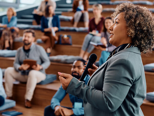 Female CEO talking while holding business presentation to group of seminar attendees at conference hall.