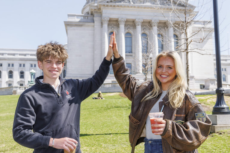 two students clap hands together in front of madison capital building