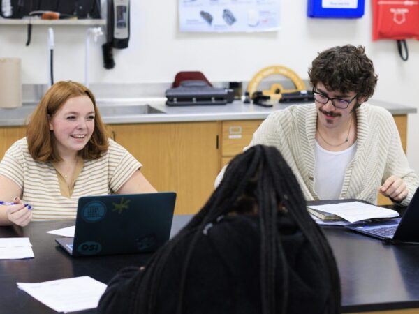 3 students at a desk talking to each other
