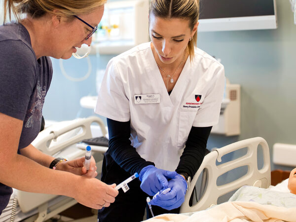 Two nurses practicing giving IV to mannequin