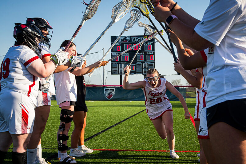 students holding up lacrosse sticks while one runs under