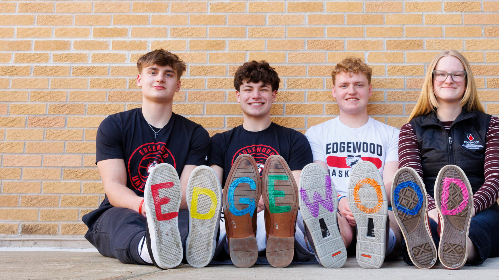 four students sitting down with Edgewood spelled out at the bottom of their shoes