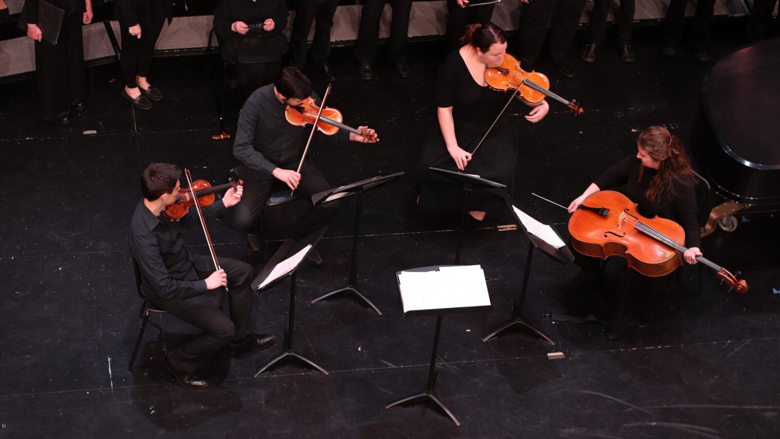 String quartet performing on stage with choir in the background