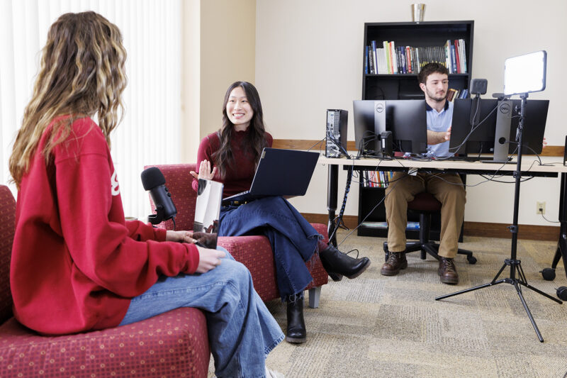 2 students talking to each other and another student using the computer
