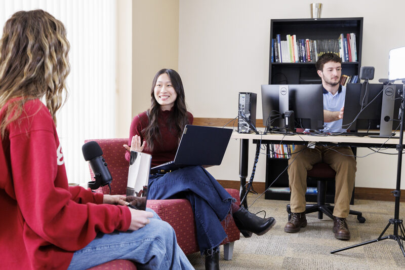 2 students talking to each other and another student using the computer